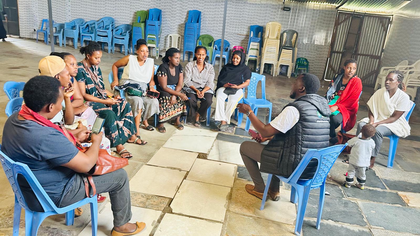 Building Resilience: Women Savings Initiative in Kitengela A group of women seated in a circle in Kitengela during a Sebineza Care Organization savings group meeting, discussing contributions and support.